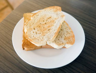 İki dilim ekmek ahşap masa üzerinde beyaz plaka tost