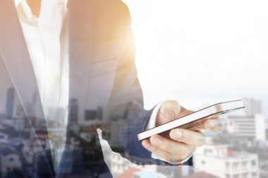 Smartphone kullanarak iş adamı. Şehir manzaralı ve güneş ışığı çift pozlama