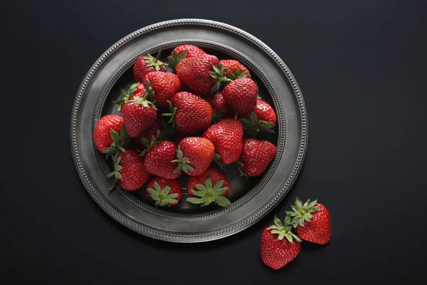 Strawberries on tin plate on black background