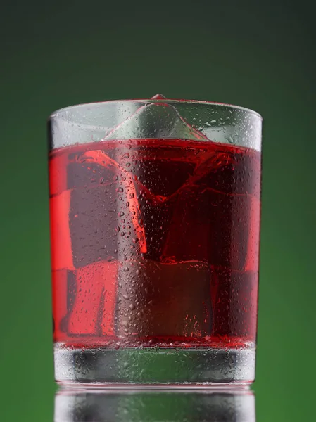 Roter Cocktail mit Eiswürfeln auf grünem Hintergrund — Stockfoto