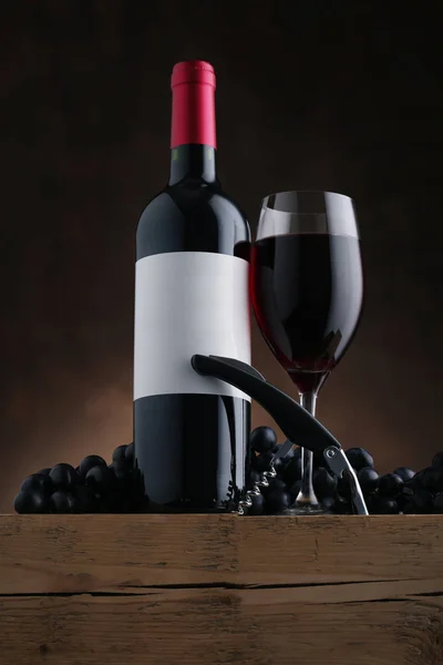 Botella de vino tinto con etiqueta y copa de vino en mesa de madera vieja — Foto de Stock