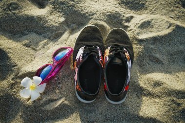Spor ayakkabı güneş gözlüğü ve frangipani sahil kumu çiçek