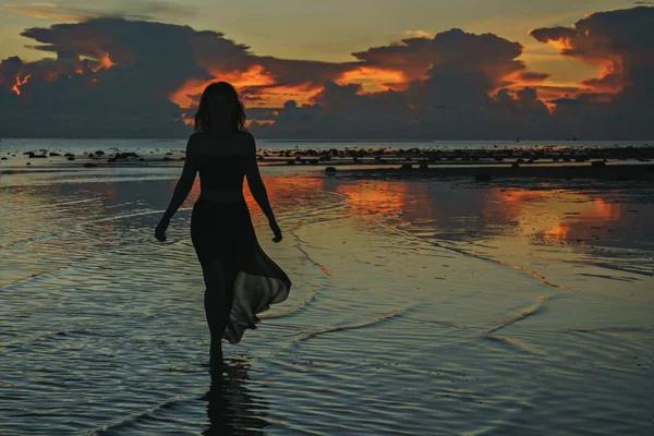 Bir uzun gün batımı renkli arka plan üzerinde sahilde dans içinde mutlu genç kadın