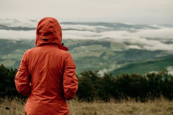 Turuncu ceketli turistin arkası. Dağların güzel manzarasına bakıyor.