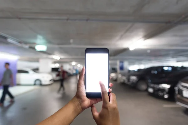 Elleri boş beyaz ekran akıllı telefon alışveriş park alanında duruyor. Bir mağaza otoparkta park edilmiş bir araba bulmak için akıllı telefon holding eller.