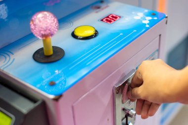 Close up hand drop a coin into game arcade machine, slot machine in selective focus. clipart