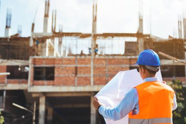 Asya adam inşaat mühendisi inşaat sitede çalışma ilerleme kontrol mavi Güvenlik kask giyiyor.
