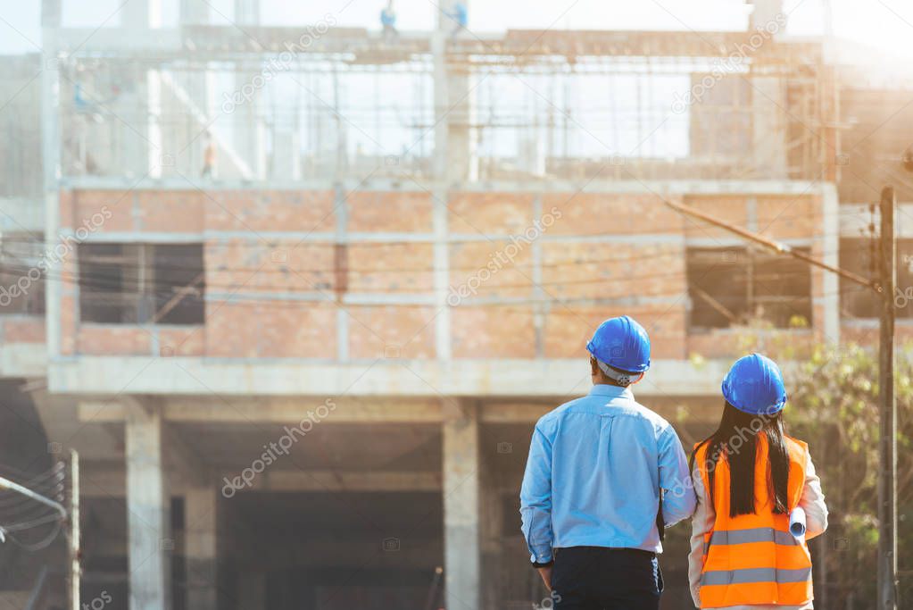 Asian man civil engineer and woman architect wearing blue safety helmet meeting at contruction site.