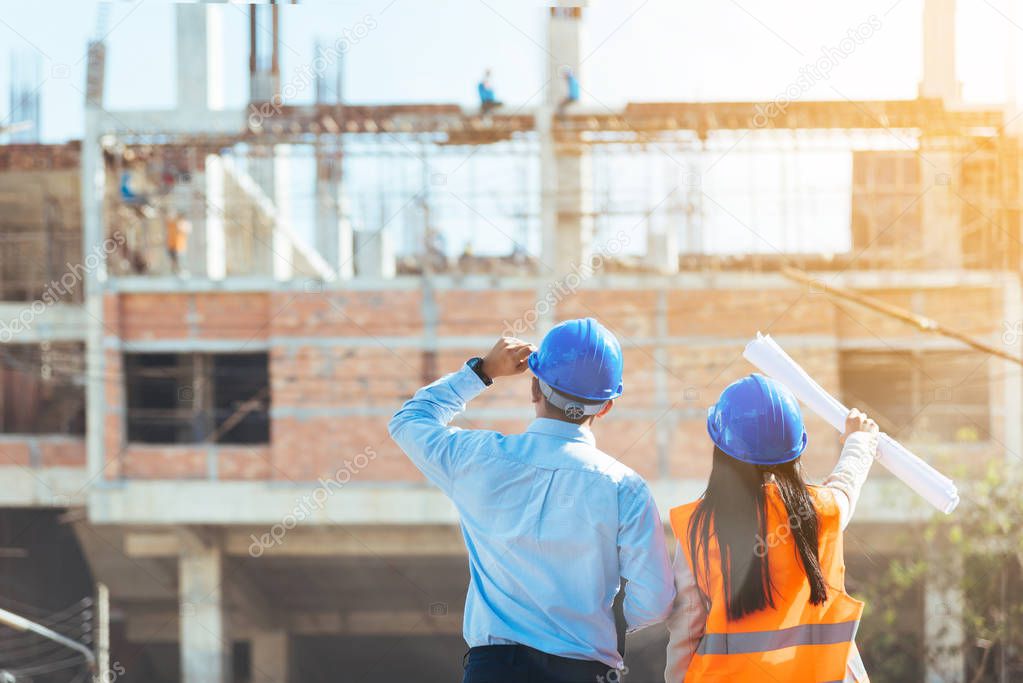 Asian man civil engineer and woman architect wearing blue safety helmet meeting at contruction site.