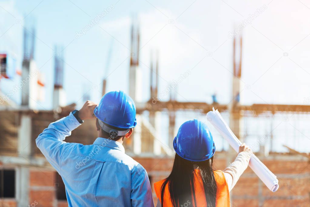 Asian man civil engineer and woman architect wearing blue safety helmet meeting at contruction site.