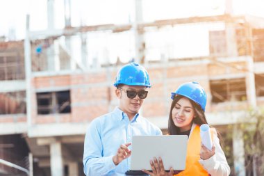 Mavi Emanet kask toplantı planları ve laptop ile inşaat sahasında ile Asya erkek ve kadın mühendis.
