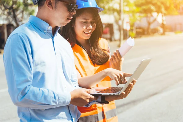 Mavi Emanet kask toplantı planları ve laptop ile inşaat sahasında ile Asya erkek ve kadın mühendis.