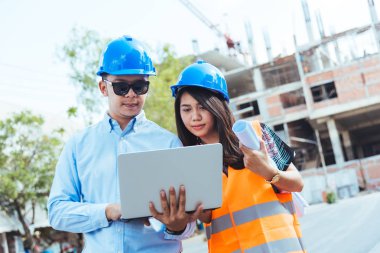 Mavi Emanet kask toplantı planları ve laptop ile inşaat sahasında ile Asya erkek ve kadın mühendis.