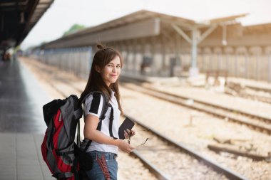 Tren istasyonunda bir tren için bekleyen kırmızı sırt çantası ile Asya kadın turist.