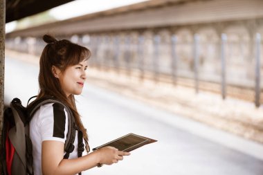 Tren istasyonunda tren beklerken tablet kullanarak mutluluk hissi Asyalı kadın gezgin.