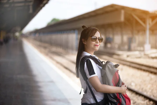 Asiatische Touristin mit rotem Rucksack wartet am Bahnhof auf einen Zug — Stockfoto
