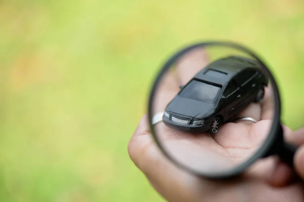 Nahaufnahme der Hand einer Person, die das Vergrößerungsglas über das schwarze Auto hält, Konzept: Finden, auswählen, reparieren — Stockfoto