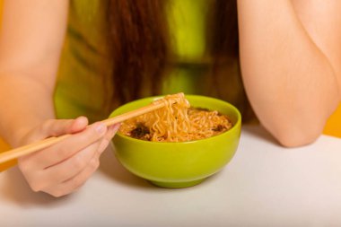 Yakın plan kadın elleri yemek çubuklarıyla hazır erişte tutuyor. Sarı arka planda stüdyo fotoğrafı.