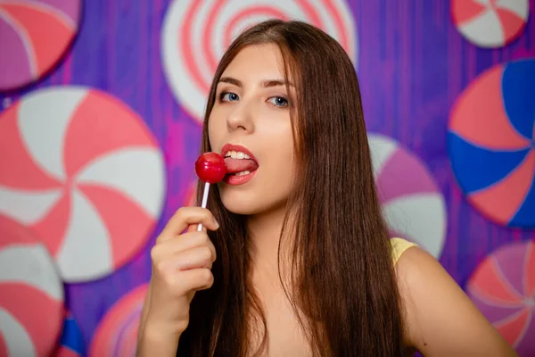 Portrait of an attractive woman with a lollipop in her hands on a background of abstract wall made of sweets.
