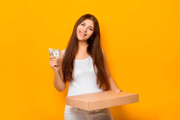 Beautiful, young woman in white clothes holding money and a box of pizza in her hands.