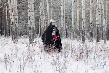 Ortaçağ savaşçısı zırhlı, miğferli, elinde kılıçla ormanda yürüyen siyah pelerinli..