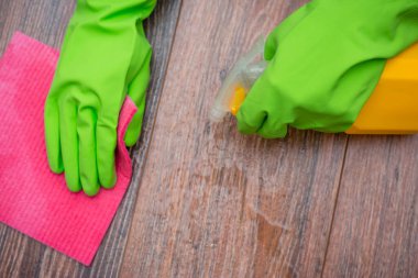 Elleri lastik eldivenli, elinde bir sprey ve ıslak temizleme bezi tutan eller. Binanın dezenfekte edilmesi, viral ve bakteriyel hastalıkların önlenmesi. Ahşap yüzeylerin temizlenmesi.