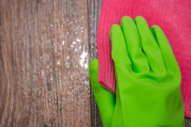 Islak ahşap bir yüzeyi ovuşturan yeşil lastik eldivenli bir elin yakın çekimi. Binanın dezenfekte edilmesi, viral ve bakteriyel hastalıkların önlenmesi. Tahta yüzeyleri temizliyorum..