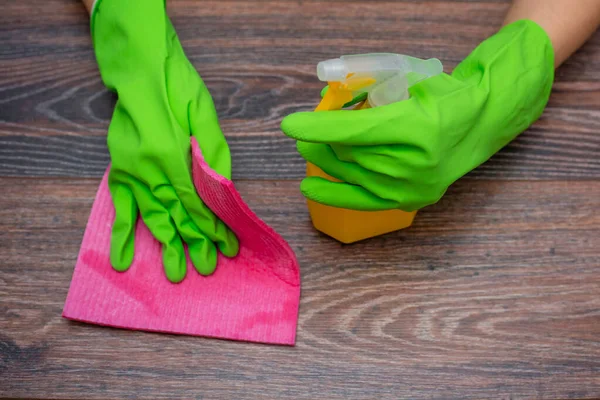 Close-up of hands in rubber gloves holding a spray bottle and rag for wet cleaning. Concept of disinfection of premises, the prevention of viral and bacterial diseases. Cleaning of wooden surfaces.