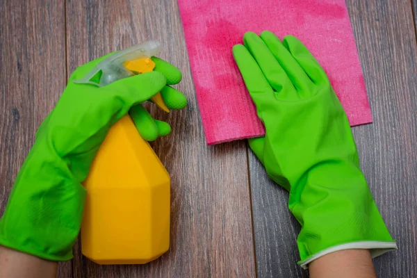 Close-up of hands in rubber gloves holding a spray bottle and rag for wet cleaning. Concept of disinfection of premises, the prevention of viral and bacterial diseases. Cleaning of wooden surfaces.