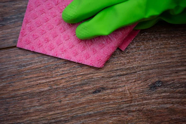 Closeup of a hand in a green rubber glove rubbing a wet wooden surface. The concept of disinfection of premises, the prevention of viral and bacterial diseases. Cleaning wooden surfaces.