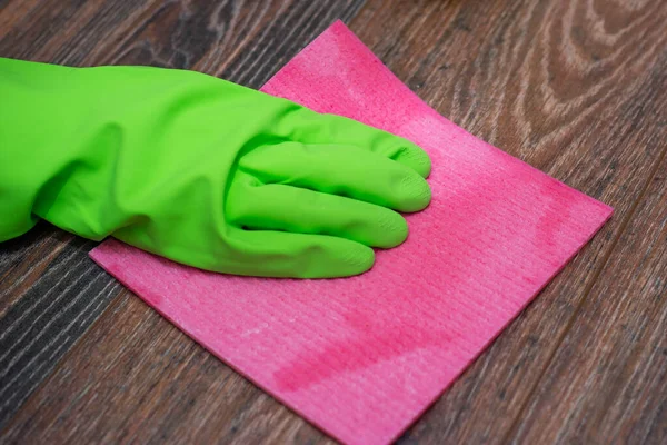 Closeup of a hand in a green rubber glove rubbing a wet wooden surface. The concept of disinfection of premises, the prevention of viral and bacterial diseases. Cleaning wooden surfaces.