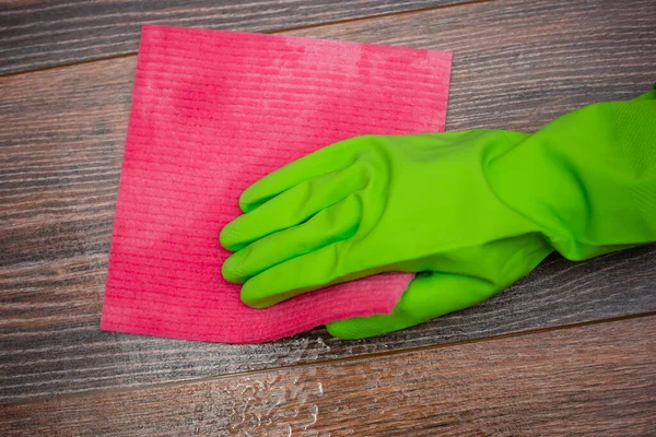 Closeup of a hand in a green rubber glove rubbing a wet wooden surface. The concept of disinfection of premises, the prevention of viral and bacterial diseases. Cleaning wooden surfaces.