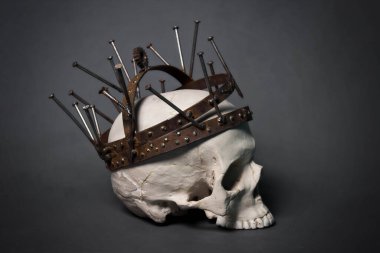 Paslı bir taç içinde çivi, dişli ve metal bantlardan yapılmış bir insan kafatası. Gri arka planda bir fotoğraf. Kıyamet sonrası, endüstriyel tarzda.