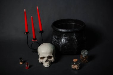 Kafatası, kazan, mumlar ve siyah arka planda malzemelerle dolu şişeler..
