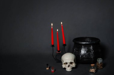 Uzayı kopyala, cadı simya seti konsepti. Kafatası, kazan, mumlar ve siyah arka planda malzemelerle dolu şişeler..