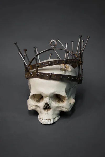 A human skull in a rusty crown, made of nails, gears and metal bands. A photo on a gray background. Postapocalypse, industrial style.