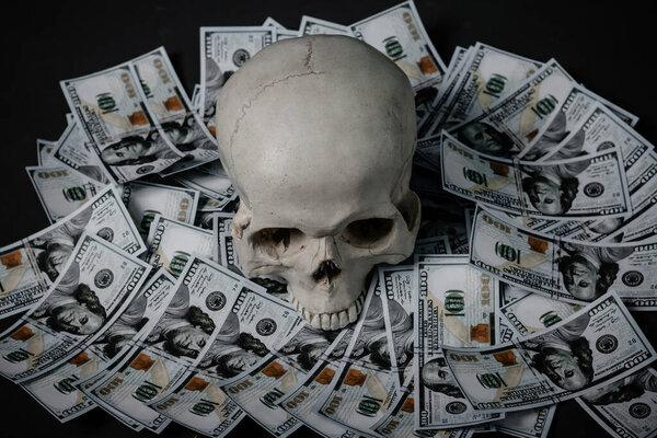 A human skull lies in the dark on money.