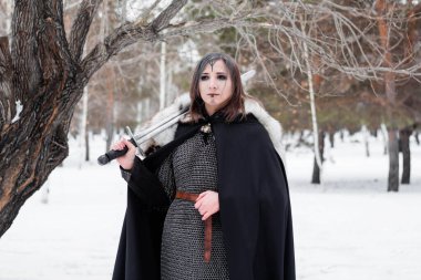  Ortaçağ kadın portresi, Viking çağının savaşçısı kış ormanlarında büyük bir ağacın arkasında. Zincirli zırh, pelerin, kürk, deri pantolon ve ellerinde kılıçla botlar. Yüzünde savaş boyası var..
