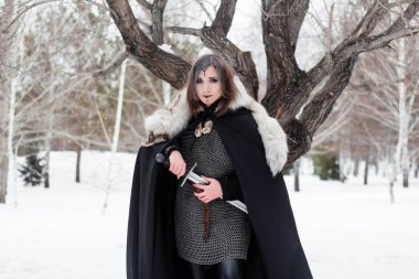  Ortaçağ kadın portresi, Viking çağının savaşçısı kış ormanlarında büyük bir ağacın arkasında. Zincirli zırh, pelerin, kürk, deri pantolon ve ellerinde kılıçla botlar. Yüzünde savaş boyası var..