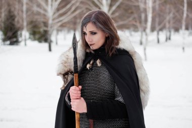 Kadın, ormanda kışın ortaçağ Viking Çağı 'nın savaşçısıdır. Zincirli zırh, pelerin, kürk, deri pantolon ve ellerinde mızrakla botlar. Yüzünde savaş boyası.