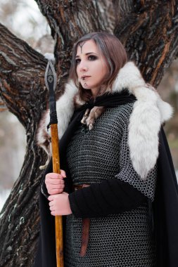Kadın, ormanda kışın ortaçağ Viking Çağı 'nın savaşçısıdır. Zincirli zırh, pelerin, kürk, deri pantolon ve ellerinde mızrakla botlar. Yüzünde savaş boyası.