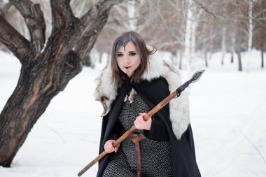 Kadın, ormanda kışın ortaçağ Viking Çağı 'nın savaşçısıdır. Zincirli zırh, pelerin, kürk, deri pantolon ve ellerinde mızrakla botlar. Yüzünde savaş boyası.