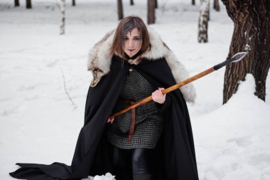 Kadın, ormanda kışın ortaçağ Viking Çağı 'nın savaşçısıdır. Zincirli zırh, pelerin, kürk, deri pantolon ve ellerinde mızrakla botlar. Yüzünde savaş boyası.