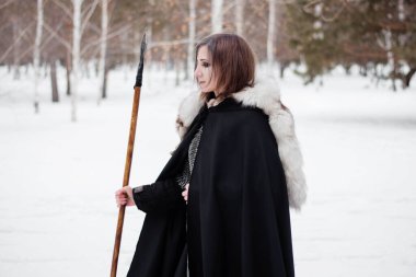 Kadın, ormanda kışın ortaçağ Viking Çağı 'nın savaşçısıdır. Zincirli zırh, pelerin, kürk, deri pantolon ve ellerinde mızrakla botlar. Yüzünde savaş boyası.
