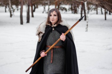 Kadın, ormanda kışın ortaçağ Viking Çağı 'nın savaşçısıdır. Zincirli zırh, pelerin, kürk, deri pantolon ve ellerinde mızrakla botlar. Yüzünde savaş boyası.