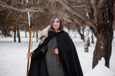 Kadın, ormanda kışın ortaçağ Viking Çağı 'nın savaşçısıdır. Zincirli zırh, pelerin, kürk, deri pantolon ve ellerinde mızrakla botlar. Yüzünde savaş boyası.