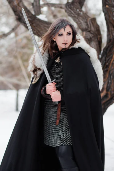 一个中世纪女人的画像 维京时代的战士在冬天的森林里 背景是一棵大树 穿着锁链邮件 皮裤和靴子 手里拿着一把剑 脸上的战斗油漆 — 图库照片