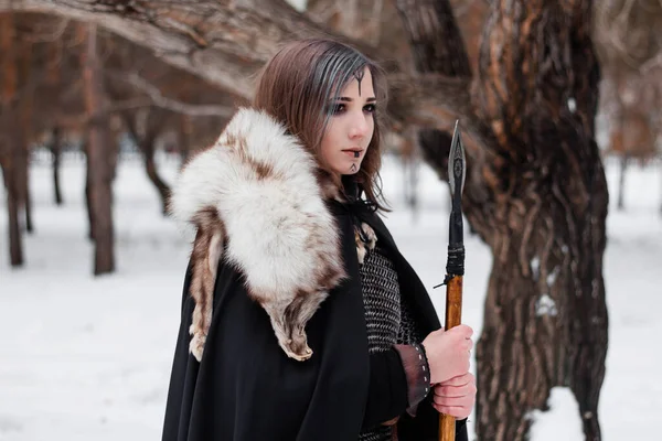 这个女人是一个中世纪的维京时代的战士 冬天在森林里 穿着锁链邮件 皮裤和靴子 手里拿着长矛 脸上的战斗色彩 — 图库照片
