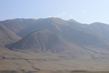 Mavi gökyüzüne karşı sisli bir dağ sırası..