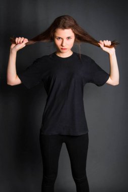 Saçını tutan siyah elbiseli güzel genç bir kadın. Stüdyo fotoğrafı, gri arka planda. Temiz ciltli bir model.